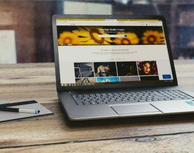 Laptop with open webpage on wooden desk, accompanied by tablet and pen, representing digital work setup.